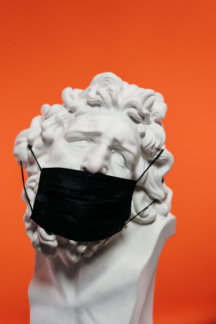 A marble bust adorned with a black face mask set against an orange background.
